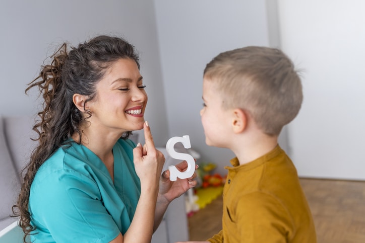 A woman teaching a child how to sound the letter S